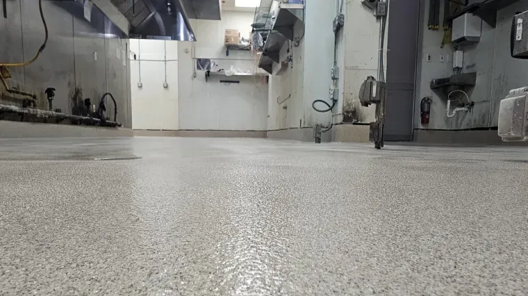 Low-angle view of a stainless-steel commercial kitchen with sinks, appliances, and a speckled floor.