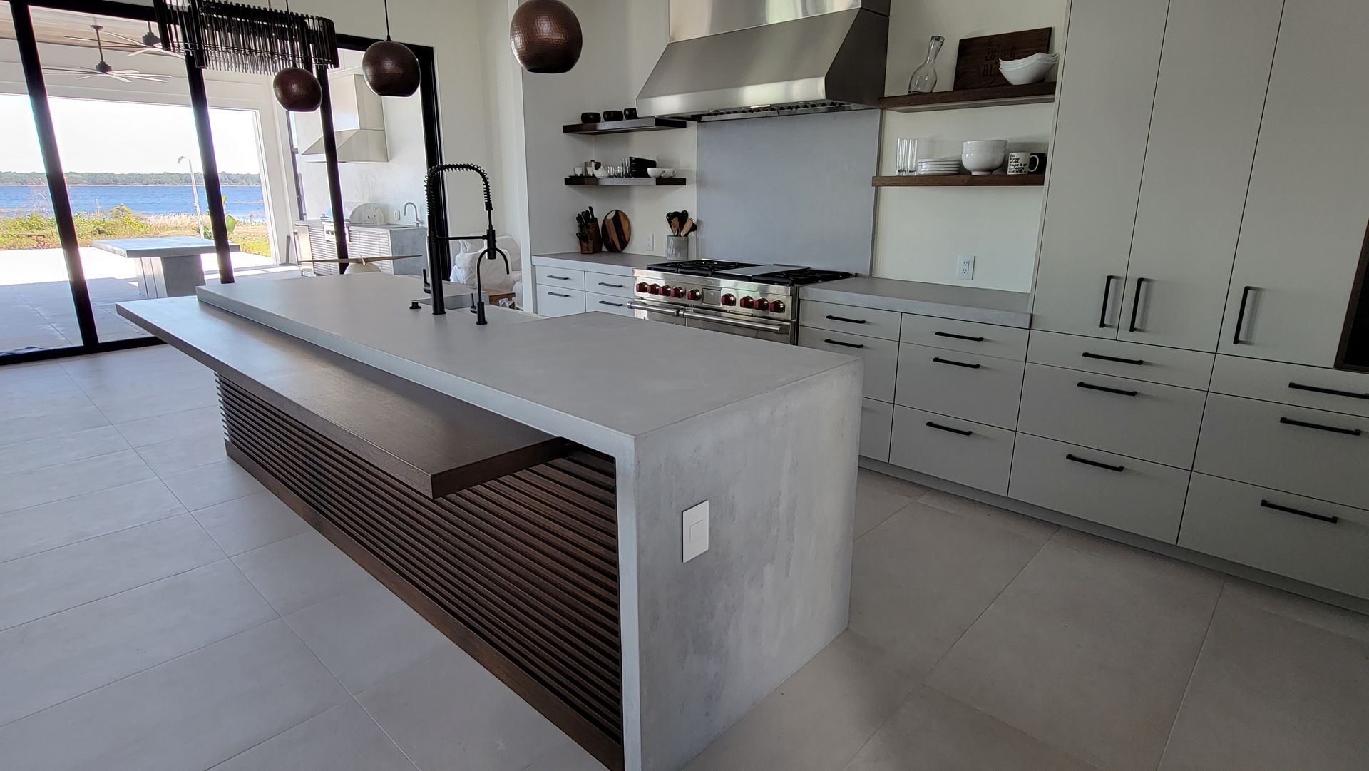 Modern kitchen with a large marble island, built-in cabinets, and floor-to-ceiling windows overlooking water.