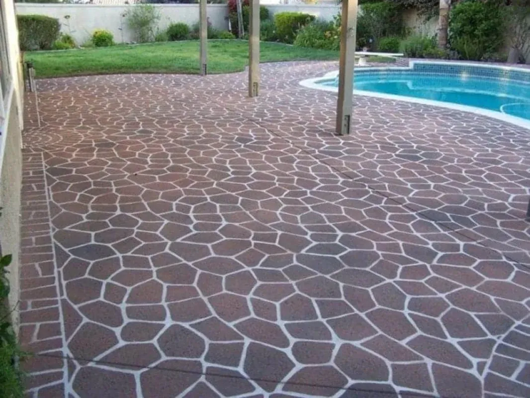 Patio with patterned stone flooring beside a swimming pool and lawn area