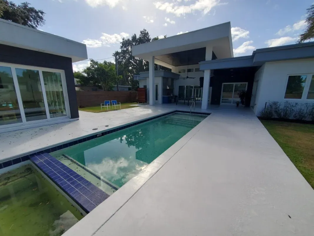 Modern house courtyard with a rectangular swimming pool and white patio beside glass doors