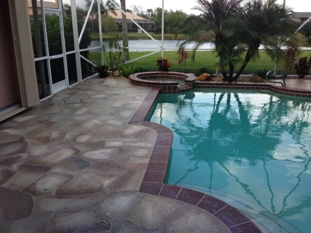 Patio beside a turquoise backyard pool with stone paving and palm trees beyond