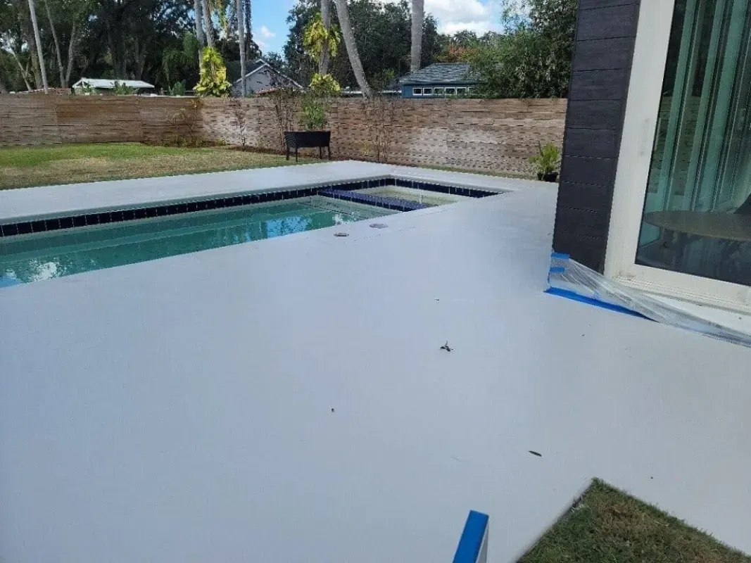 Patio with white flooring beside a swimming pool and brick wall, viewed from a glass door