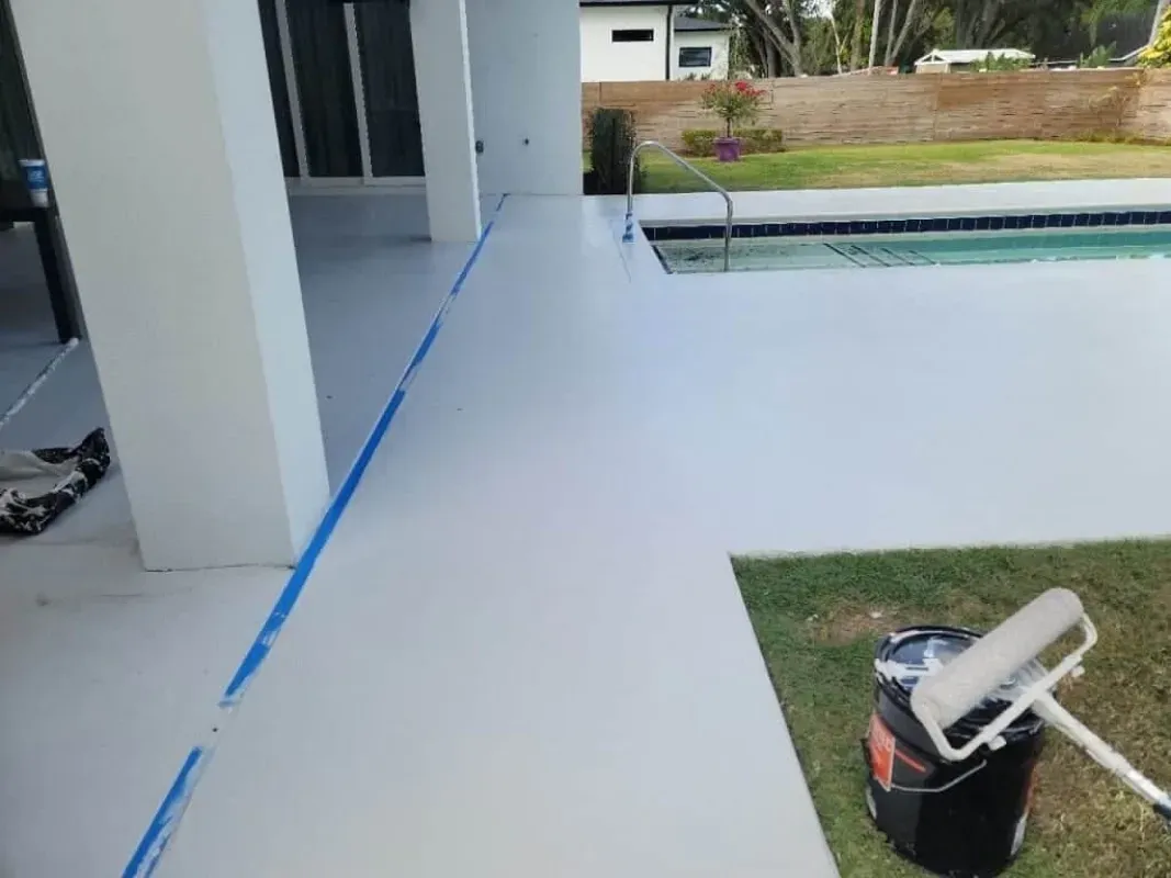 Freshly painted white patio floor beside a pool, with blue painter’s tape along the edge.