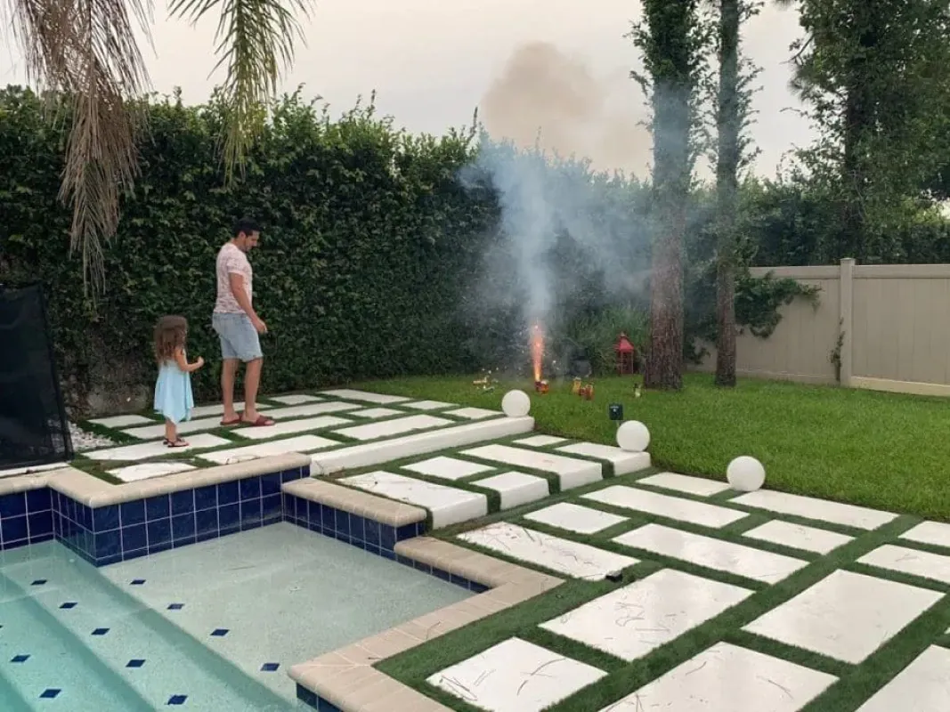 Backyard pool with white stepping stones, smoke rising, and two people standing by the poolside