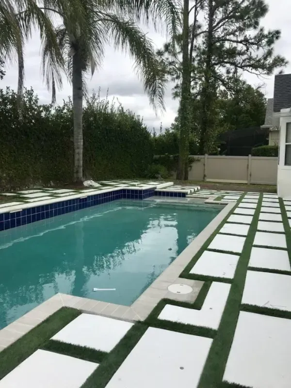 Backyard pool with white-tiled patio, blue water, palm trees, and hedge fencing