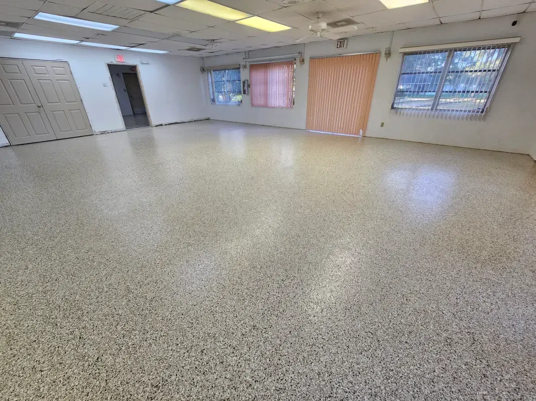 Empty carpeted room with white walls, windows, and fluorescent ceiling lights