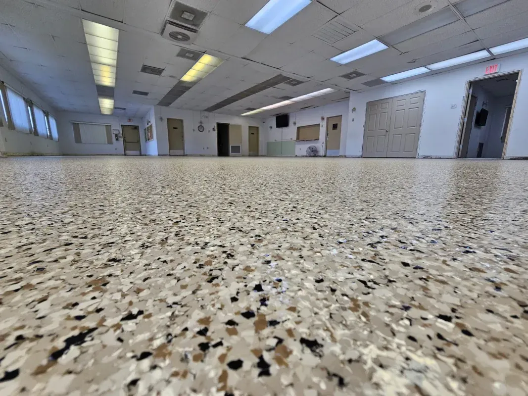 Empty hallway with speckled floor, fluorescent ceiling lights, and doors along both walls