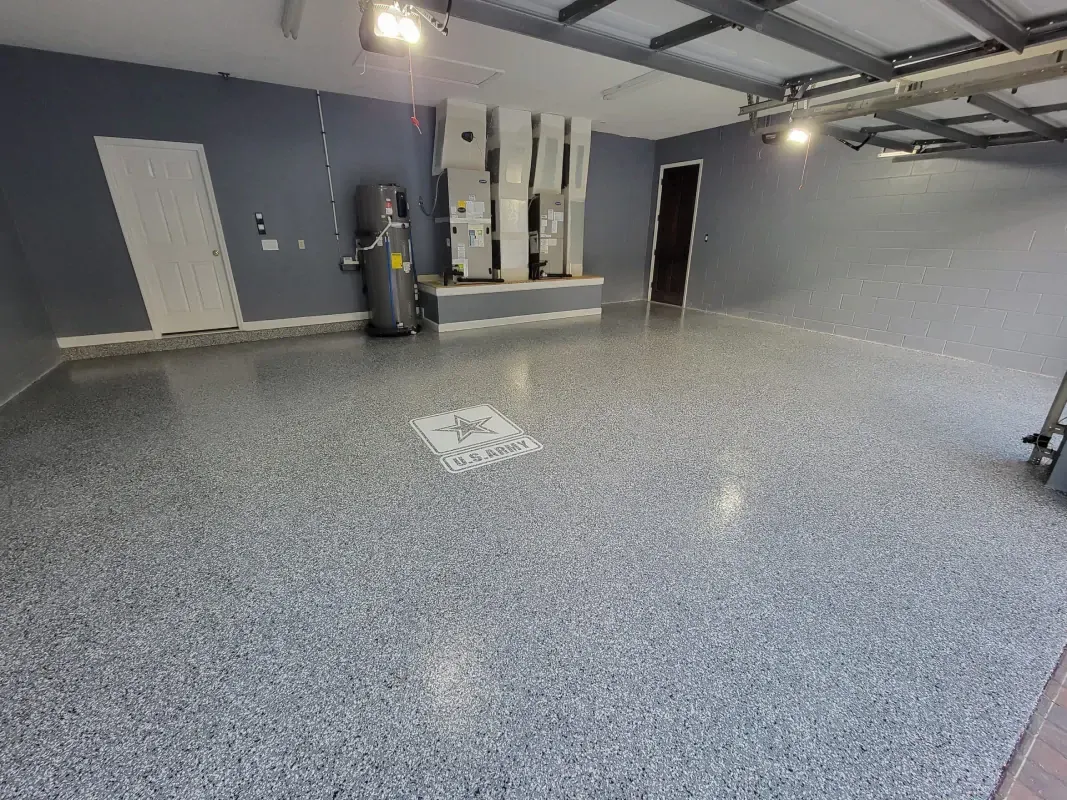 Empty gray garage with speckled floor, wall-mounted equipment, and a doorway at the back.
