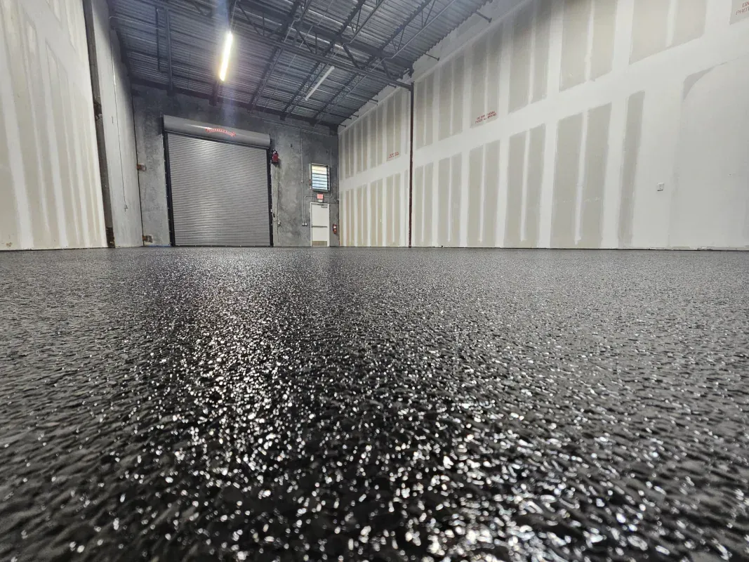 Low-angle view of a wet, speckled floor in an industrial hallway with unfinished walls and a closed door.