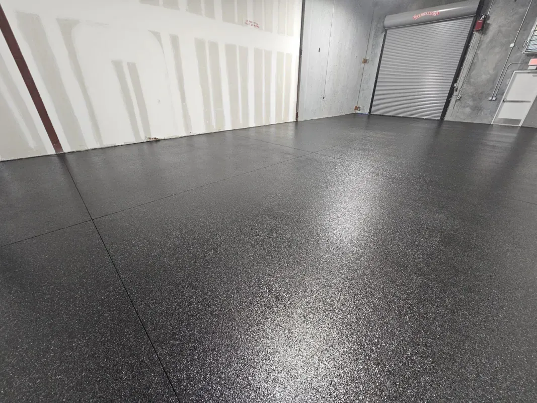 Empty storage unit with dark speckled epoxy floor and white walls under bright light.