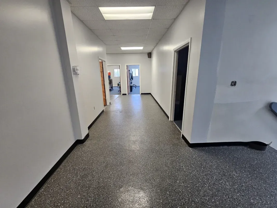 Long white hallway with speckled floor, doorways, and a person near the far end