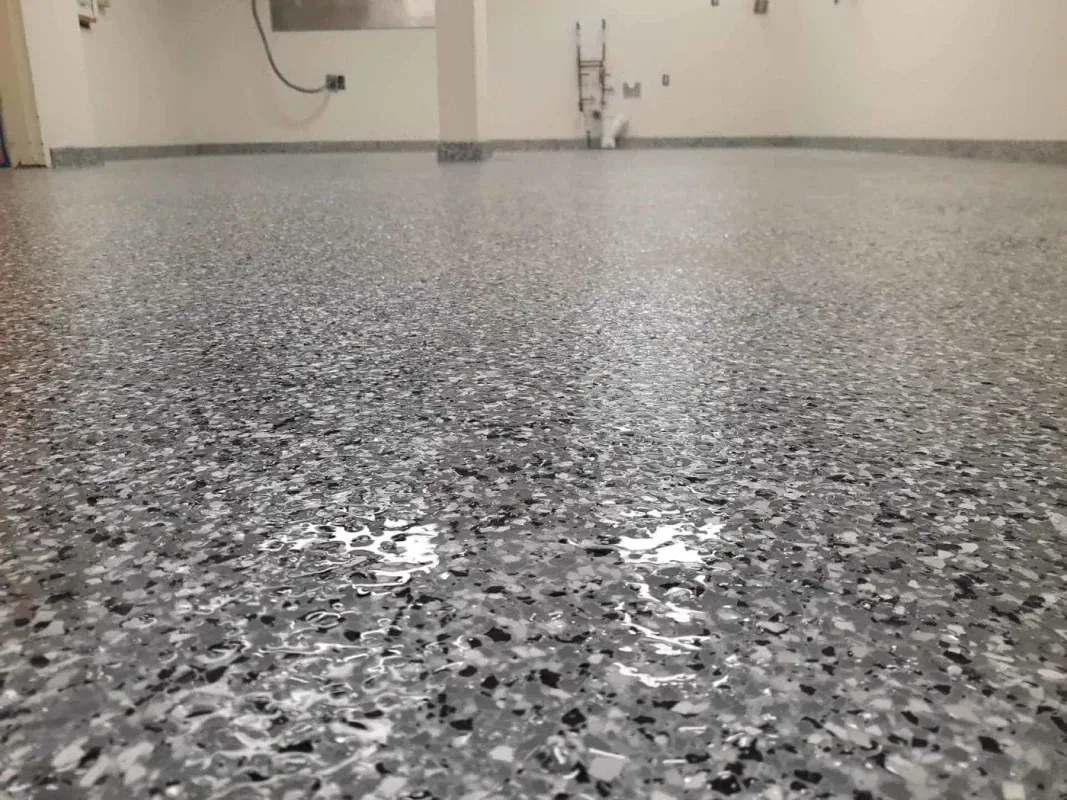 Low-angle view of a gray speckled floor in an empty room with a sink and pipes along the back wall