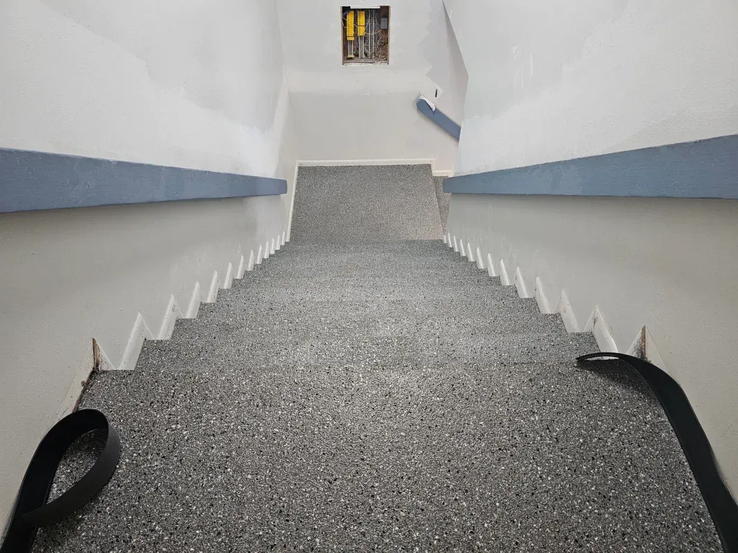 Stairwell with white walls, blue trim, and a gray carpeted ramp leading to a small window.