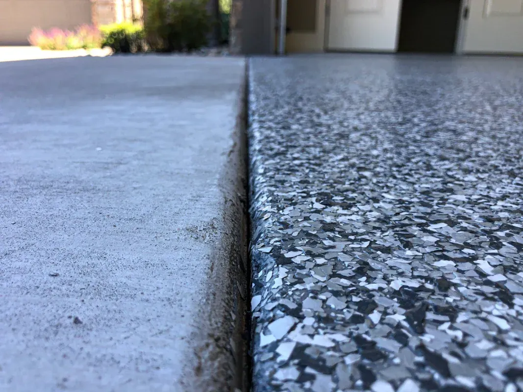 Close-up of a concrete expansion joint between smooth and speckled pavement, with a building blurred in the background