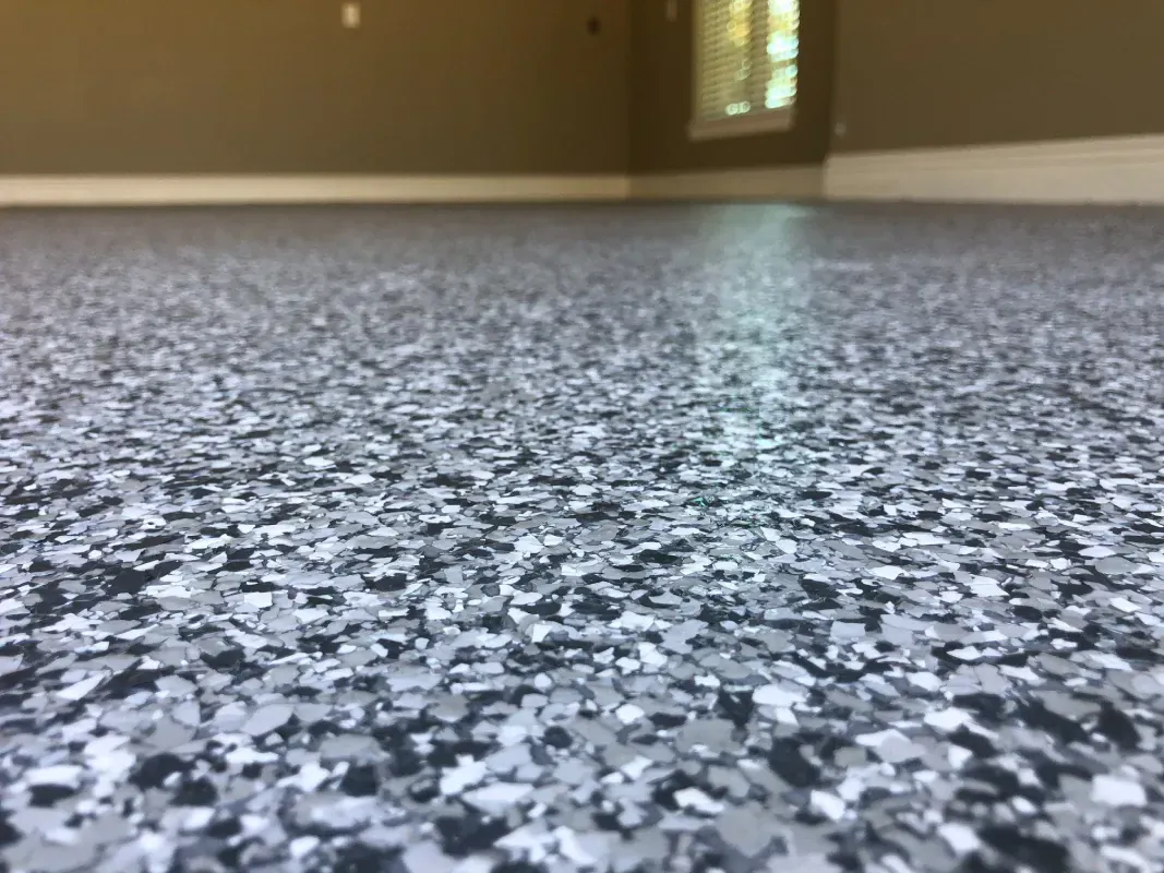 Low-angle view of a speckled gray floor in an empty room with a distant window and beige walls