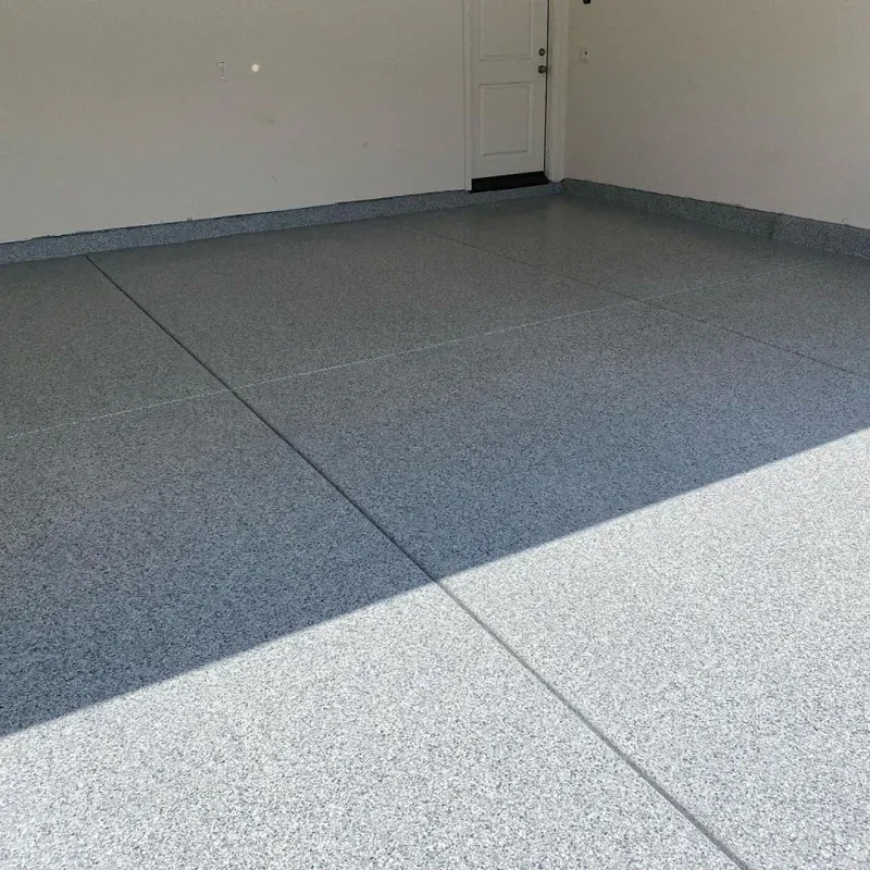 Empty garage with gray speckled floor and a closed white door in the back corner