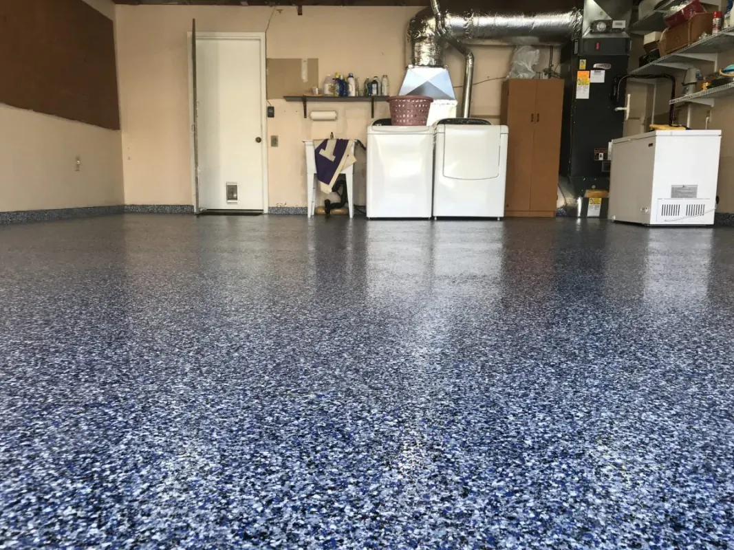 Empty garage with speckled epoxy floor, washer and dryer, storage cabinets, and exposed ductwork.