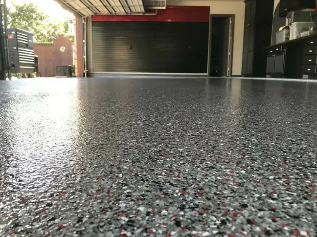 Low-angle view of a speckled garage floor facing an open garage door and red car lift.