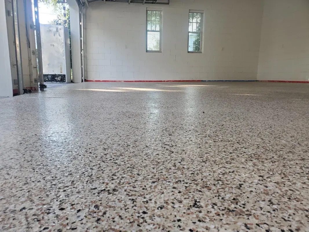 Empty tiled room with speckled floor, white walls, and small windows.
