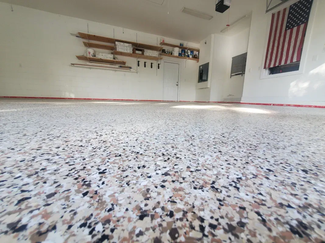 Empty garage interior with speckled floor, wall shelves, and an American flag on the right side.