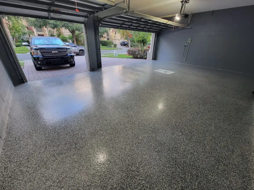 Spacious epoxy-floored garage with a parked black truck and open door to the driveway