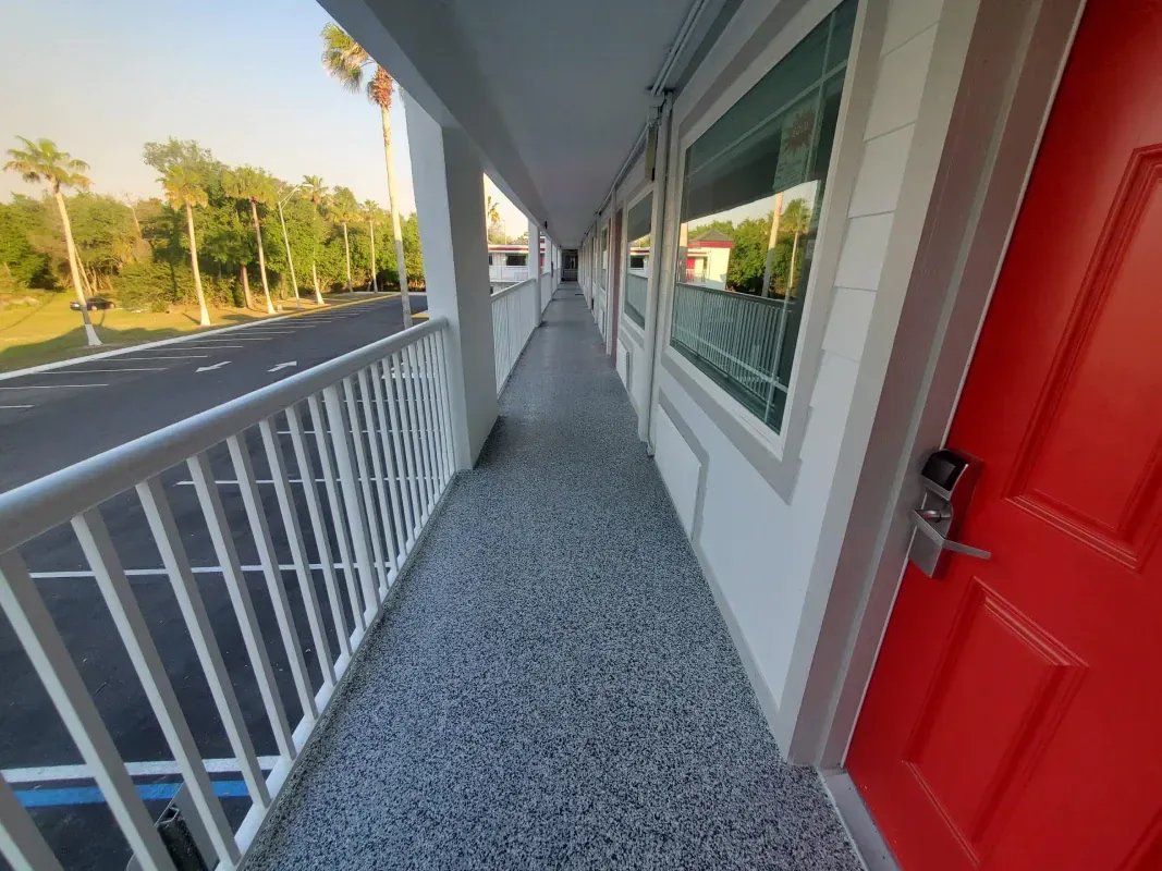 Covered motel walkway with red door, white railing, and storefront windows along a roadside.