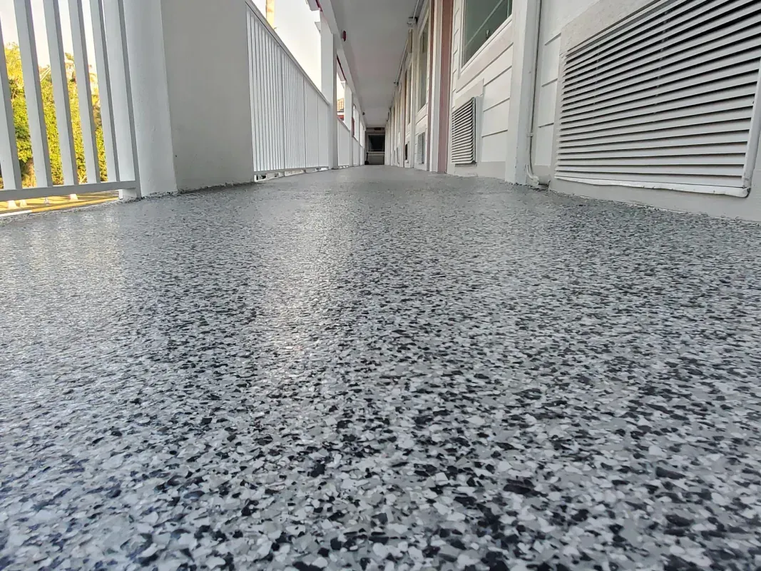 Low-angle view of a speckled gray floor in a hallway with white walls and railing.