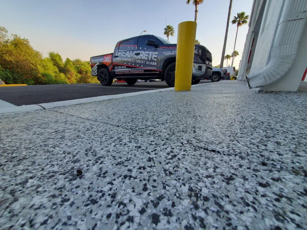 Low-angle view of a sidewalk beside parked vehicles, with a yellow bollard and palm trees in the background