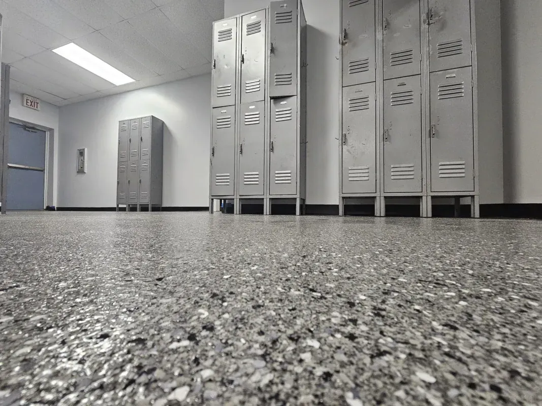 Empty school hallway with gray lockers and speckled flooring, viewed from a low angle.