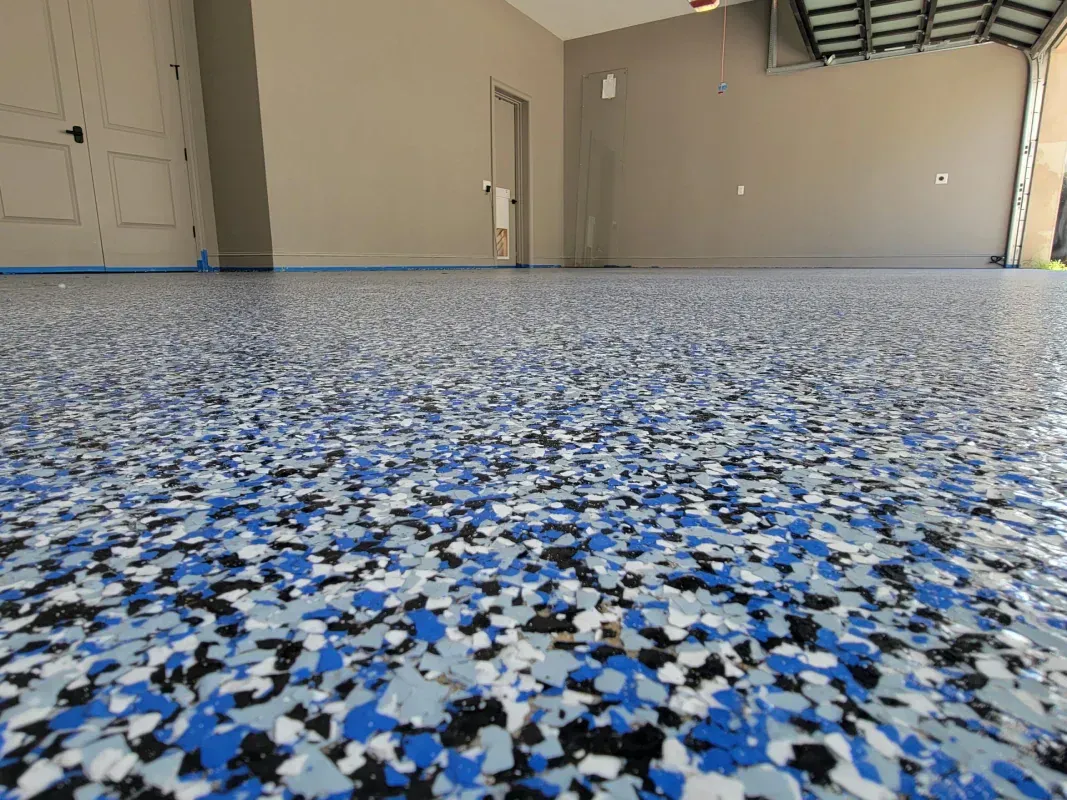 Empty garage interior with blue, white, and black speckled epoxy floor and open door.
