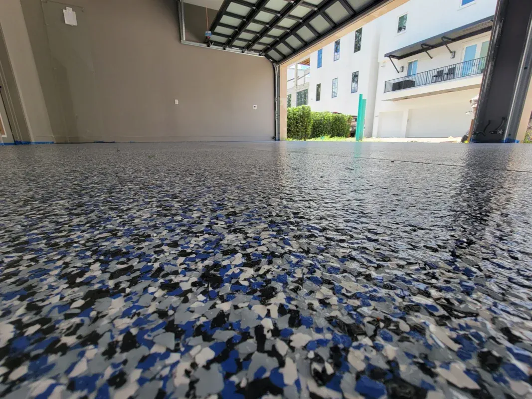 Low-angle view of a speckled garage floor with a covered driveway and apartment building in the background