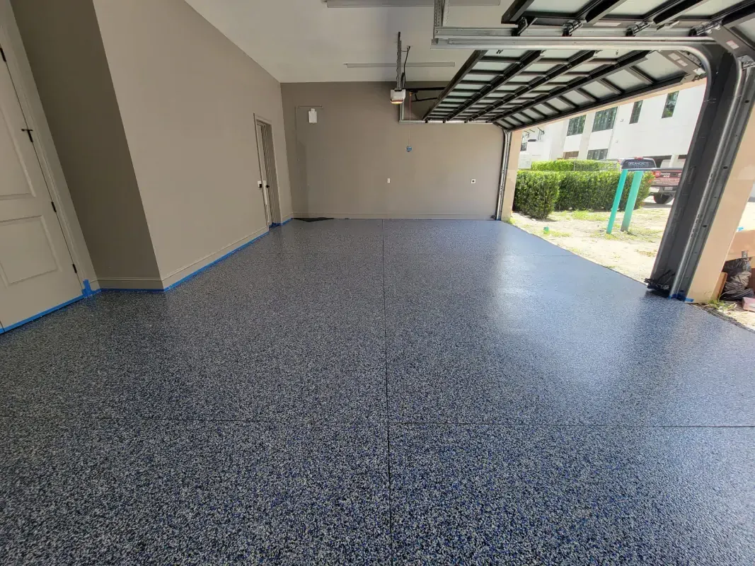 Empty garage with speckled blue-gray epoxy floor and open door to the driveway.