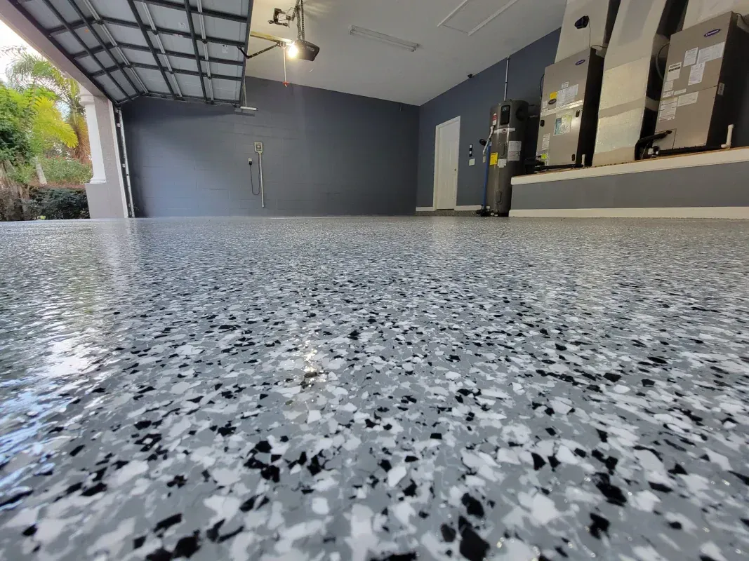 Low-angle view of a speckled epoxy garage floor with open garage and shelves in the background