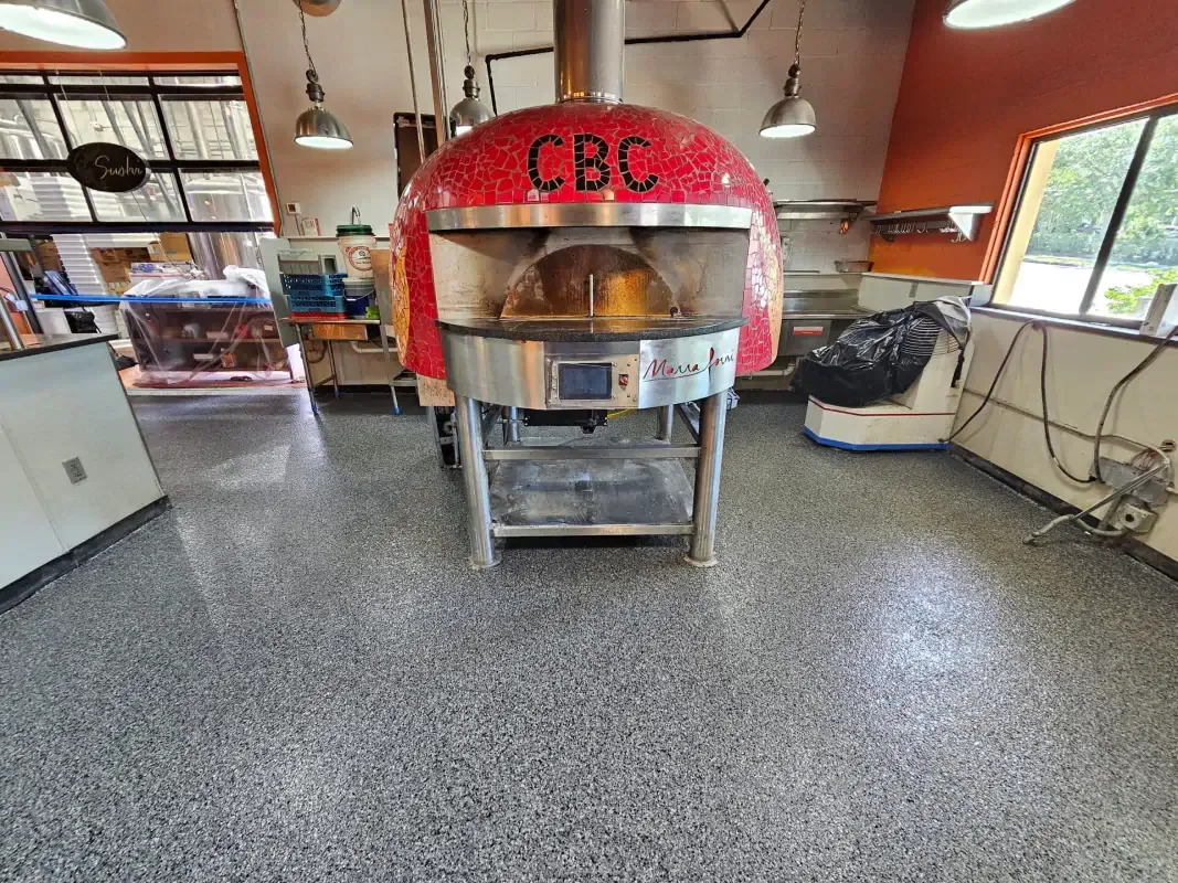 Red brick pizza oven in a restaurant kitchen with a stainless steel prep table and open shelving.