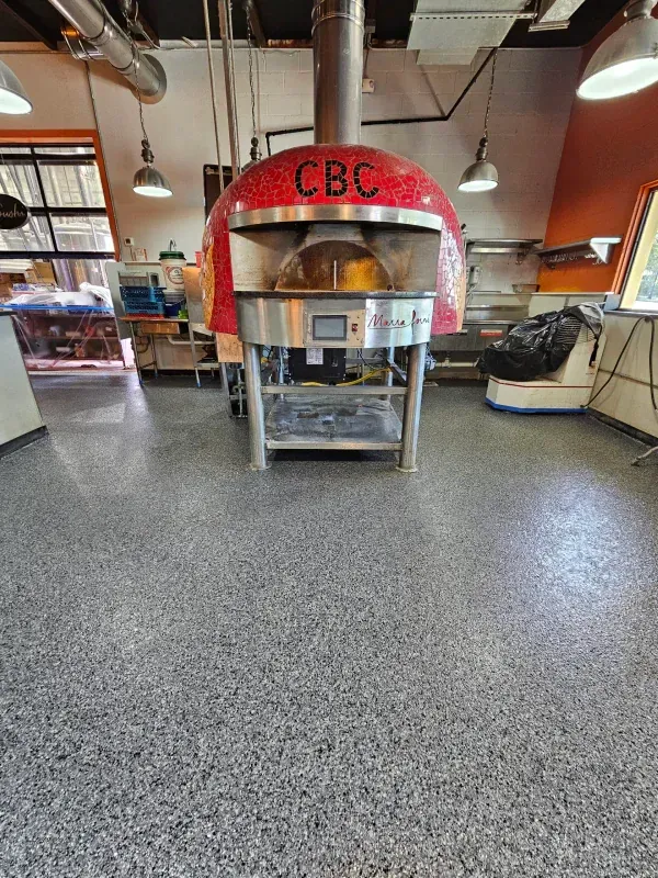 Red pizza oven on a wheeled stand in a restaurant kitchen area with gray speckled floor and hanging lights