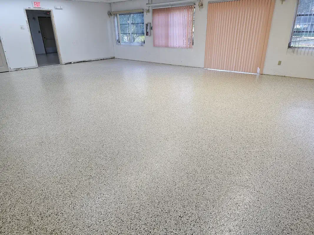 Empty indoor room with speckled floor, white walls, a door, and curtained windows.