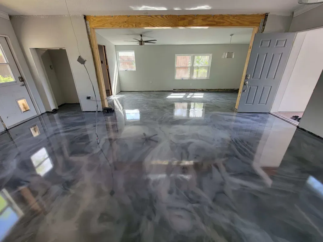 Empty garage with glossy gray concrete floor, open door, and bright windows at the back