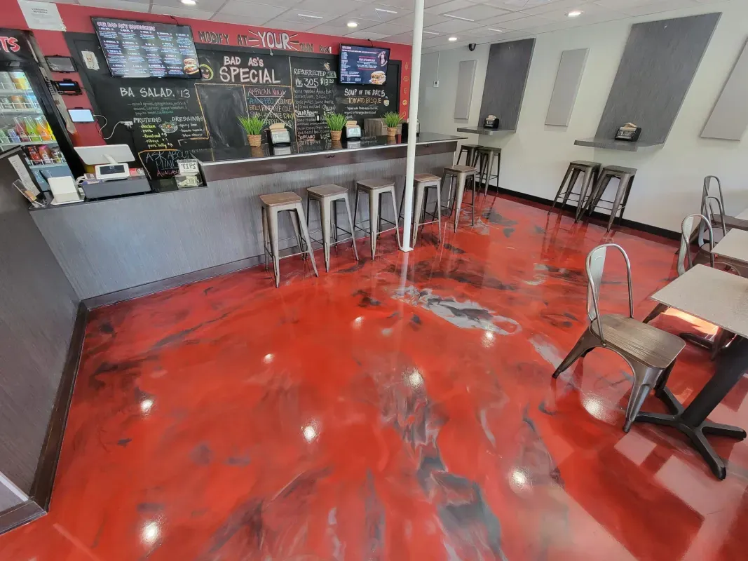 Small café interior with glossy red floor, counter, stools, and tables by the windows.