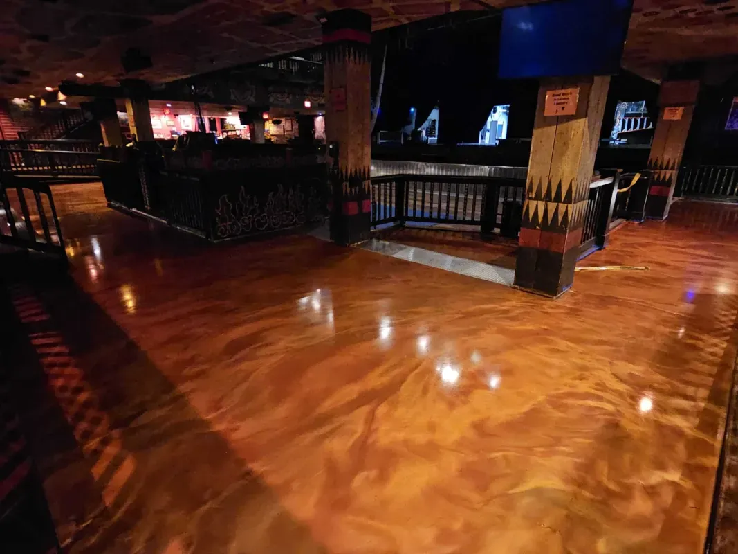 Empty polished wooden dance floor in a dimly lit nightclub or bar with tables and railings.