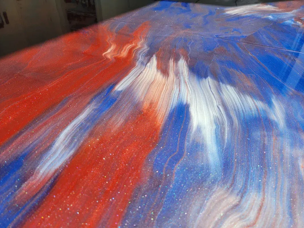 Abstract red, white, and blue paint swirls across a canvas close-up.