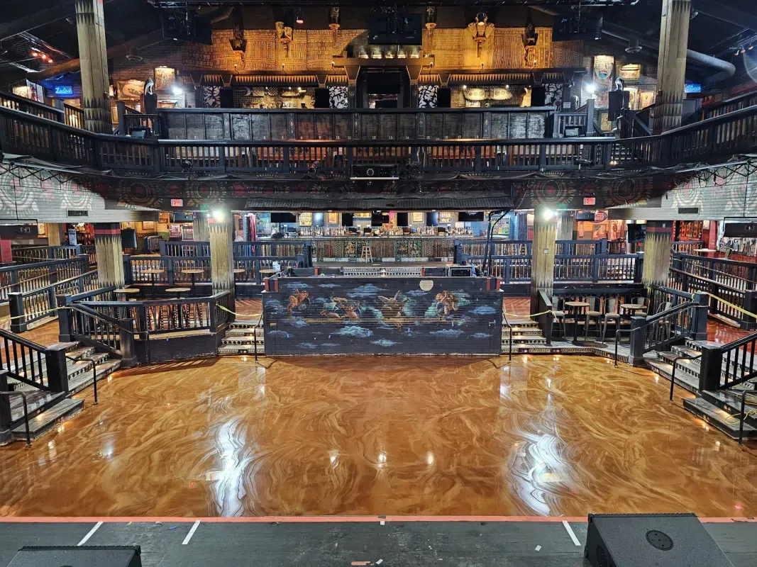 Empty nightclub dance floor with stage, bar seating, and warm amber lighting