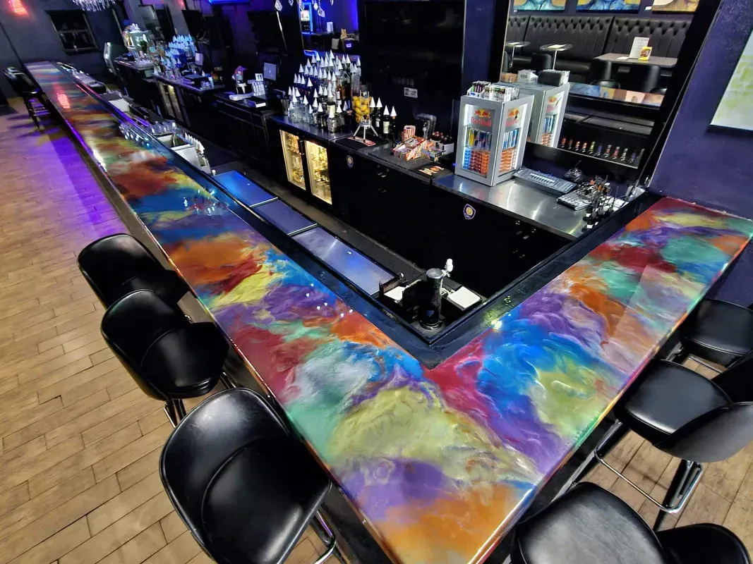 Colorful bar counter with black stools and bottles displayed along a dark lounge interior.