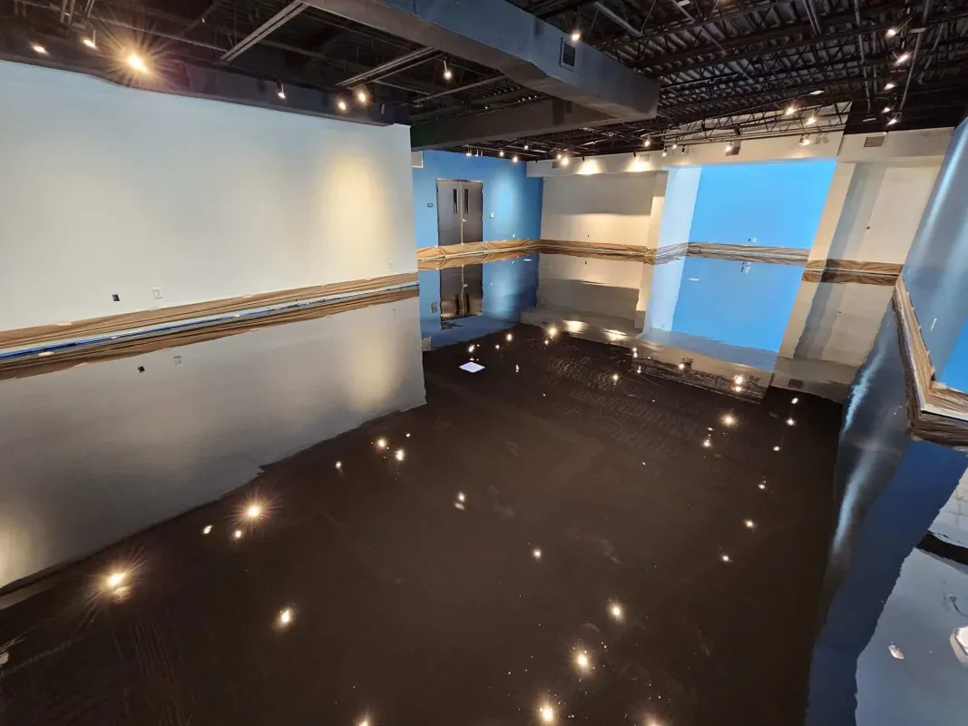 Empty modern gallery with glossy black floor, white walls, and blue accent panels