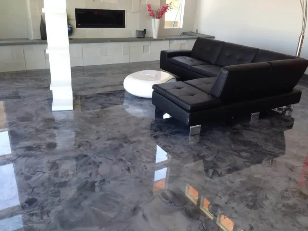 Modern living room with black leather sectional, white round ottoman, and gray marble floor.