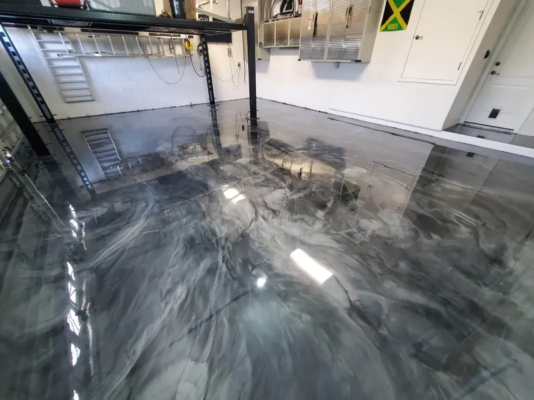 Glossy gray epoxy floor in an empty industrial room with ladders, shelves, and equipment along the walls
