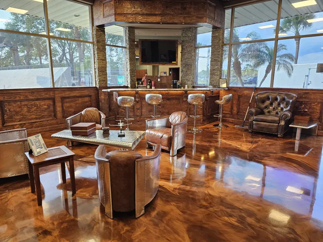 Modern lounge with leather chairs, wood table, stone fireplace, and ocean-view windows.