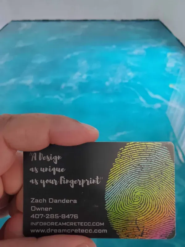 Hand holding a black business card with gold and rainbow swirls over a bright blue surface
