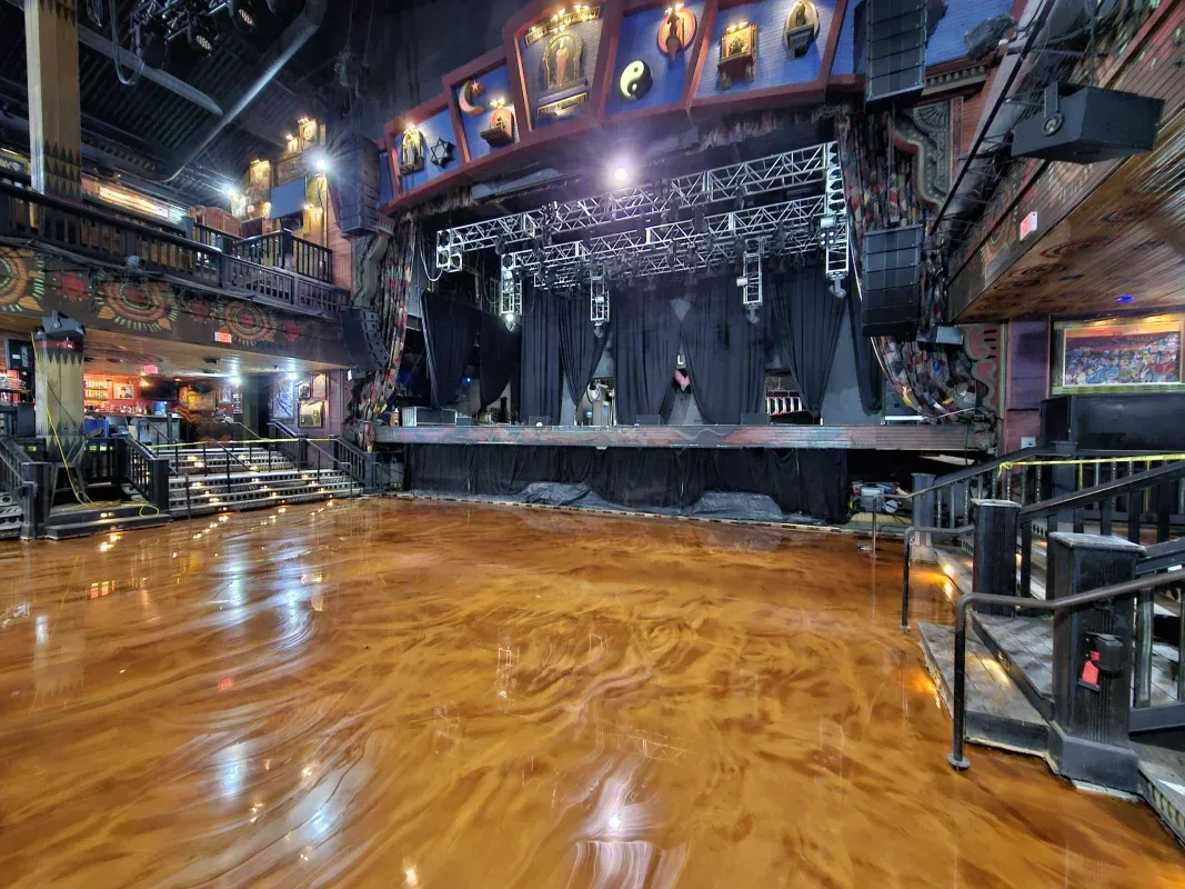 Empty nightclub with a glossy wooden floor and a lit stage under blue-purple lights.