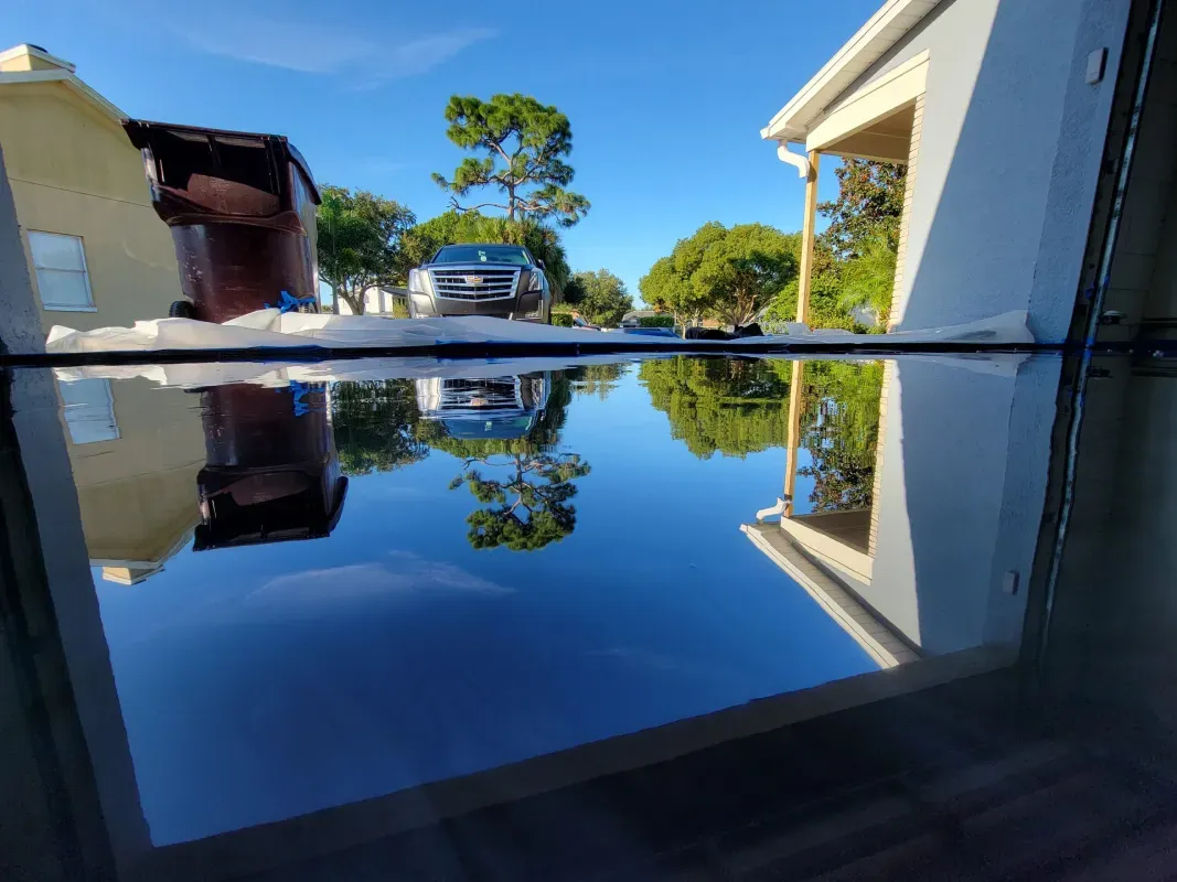 Backyard pool reflecting blue sky, trees, and house in still water