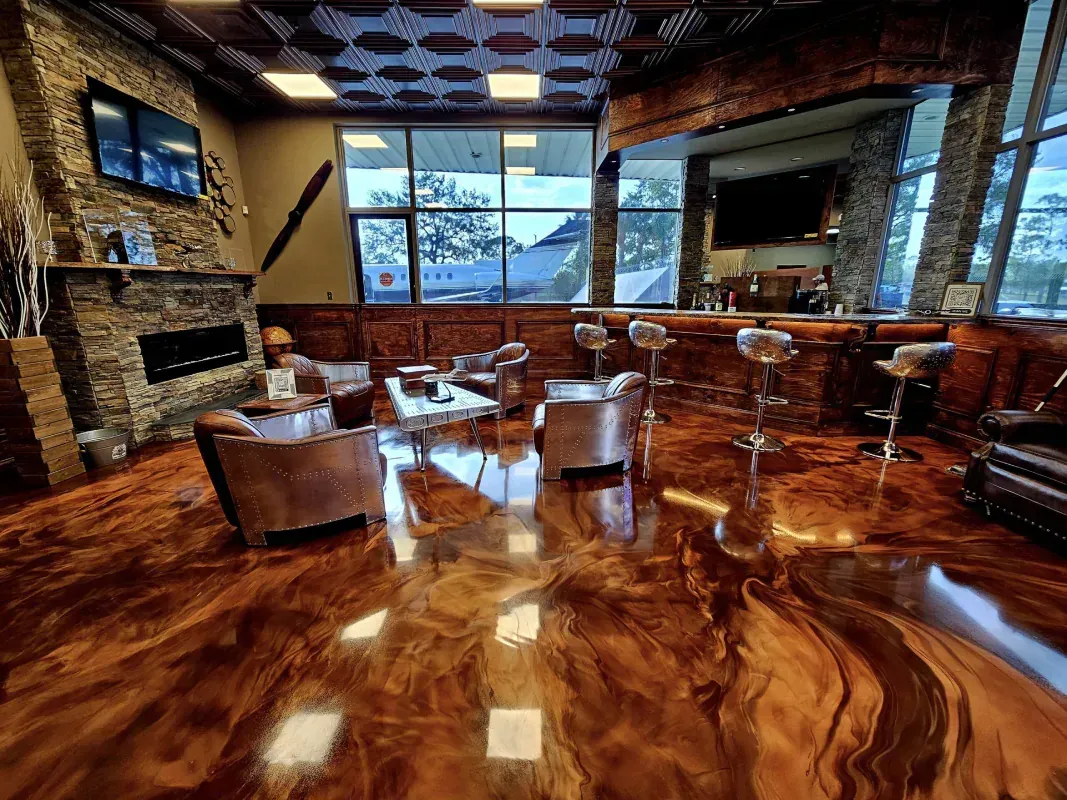 Modern lounge with glossy wood floor, leather seating, fireplace, and large window overlooking water